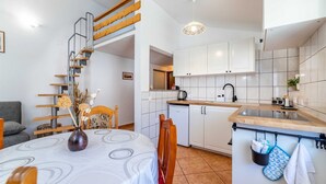 Une cuisine compacte avec des meubles blancs, une table à manger en bois et un four encastré.