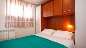 A bedroom with a bed, a window with curtains, a radiator, and a bedside lamp. - Apartment Bozo Baska on the ground floor with terrace (Baška)