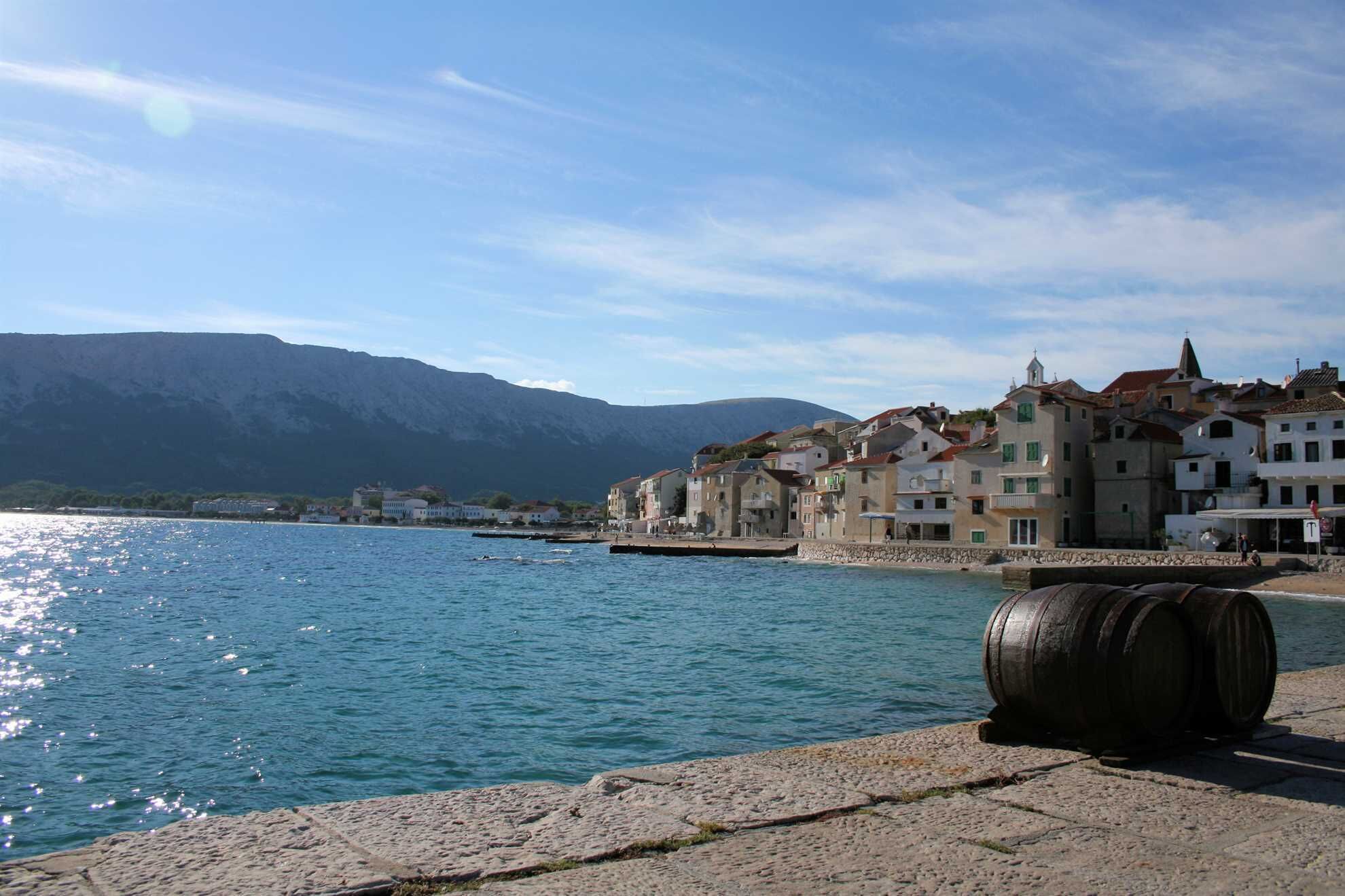 A waterfront view with buildings, a stone wall, and a barrel.