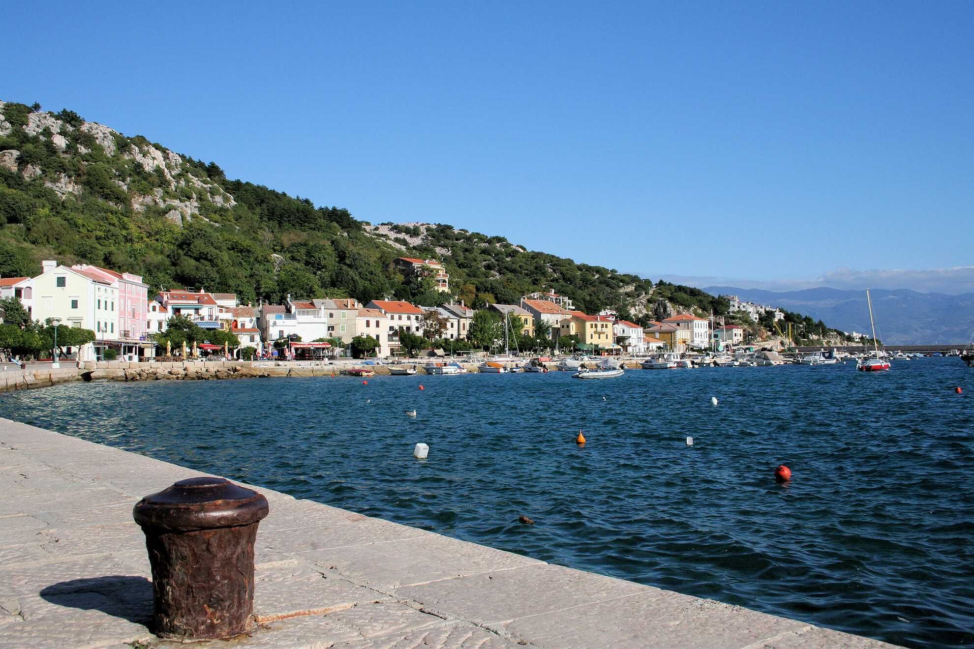 A coastal town with colorful buildings along the waterfront, boats docked, and a clear blue sky.