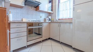 A compact kitchen with a gas stove, oven, and a window with curtains. - Family apartment Antica A4 (Baška)