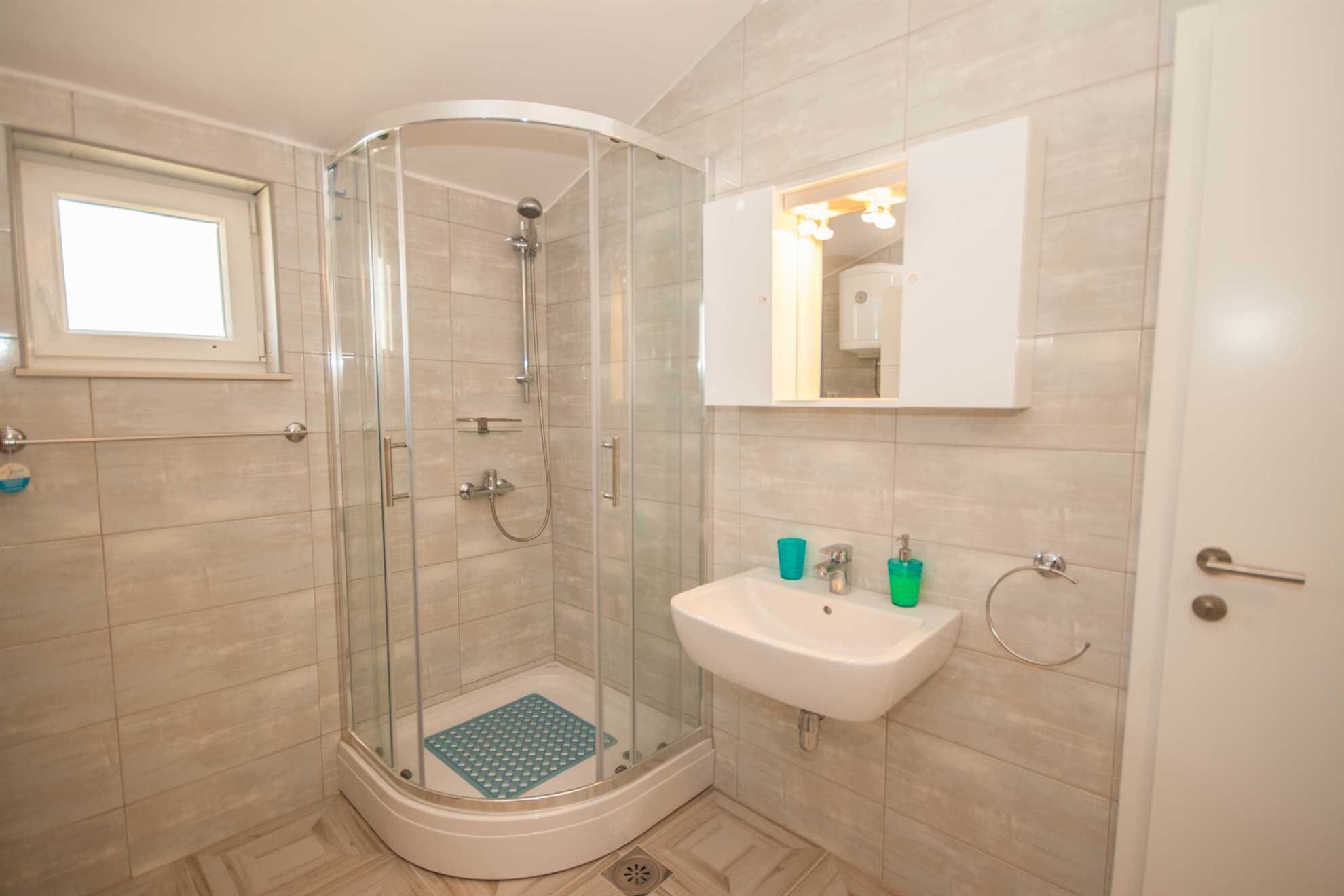 A modern bathroom with a glass-enclosed shower, a sink with a mirror above, and a window.