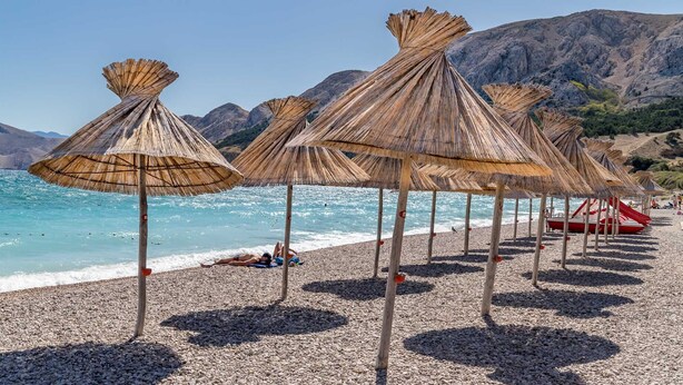 En strand med parasoller av halmtak och en strand med småsten.