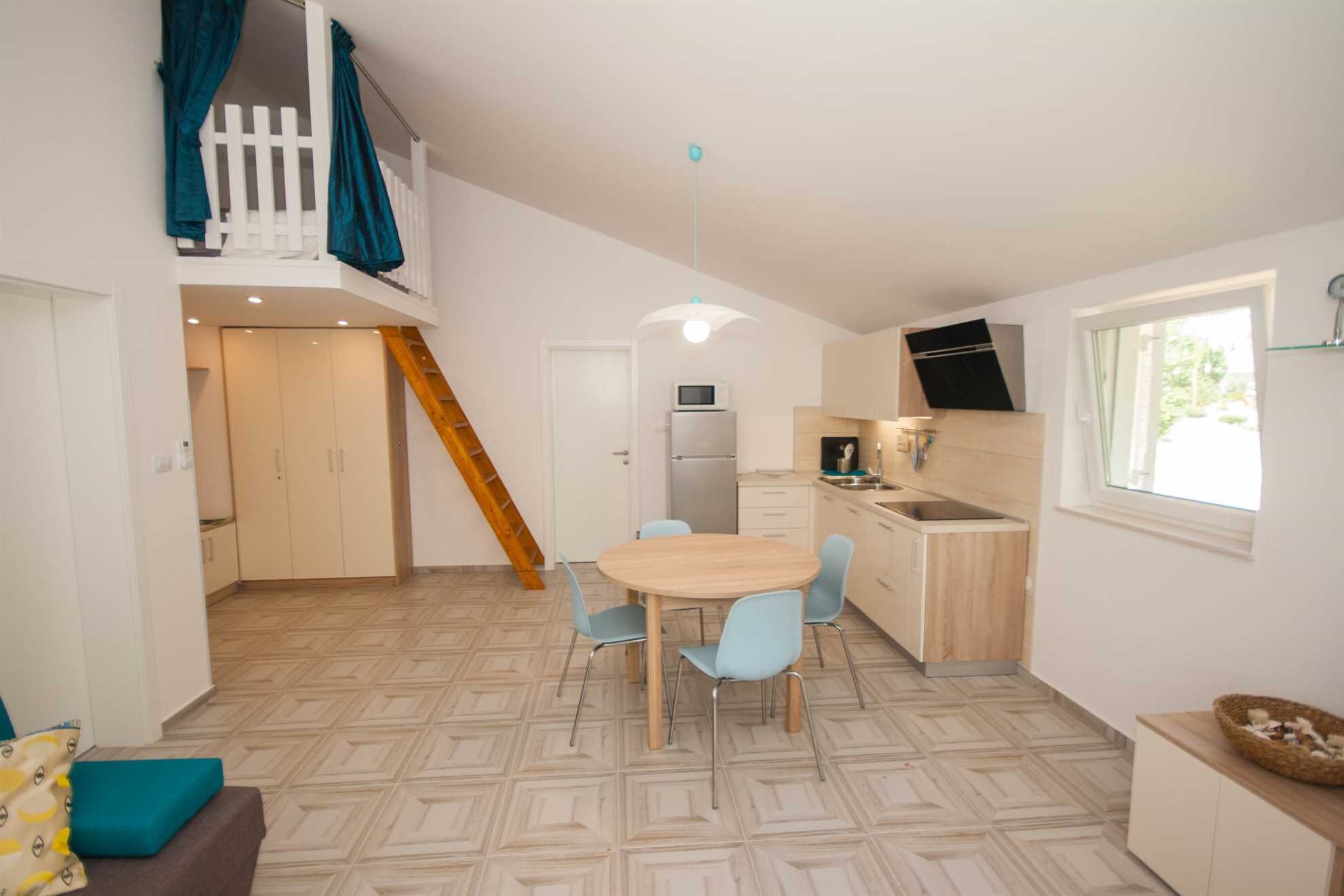 Un espace de vie compact comprenant un coin repas, une kitchenette et un escalier menant à un niveau supérieur.
