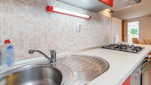 Een moderne keuken met een roestvrijstalen spoelbak, een gasfornuis en rode keukenkastjes.