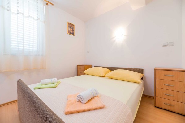 Un dormitorio con cama, dos almohadas, una mesita de noche, una silla y un armario.