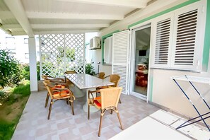 Un patio couvert avec une table et des chaises, une cloison en treillis blanc et une porte-fenêtre coulissante donnant sur la cuisine.