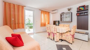Een gezellige woonkamer met een bank, een eettafel met bloemenstoelen, een televisie en een kast met planken.