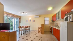 Een compacte keuken met een eethoek, met een televisie, een eettafel met stoelen, een magnetron en een koelkast.