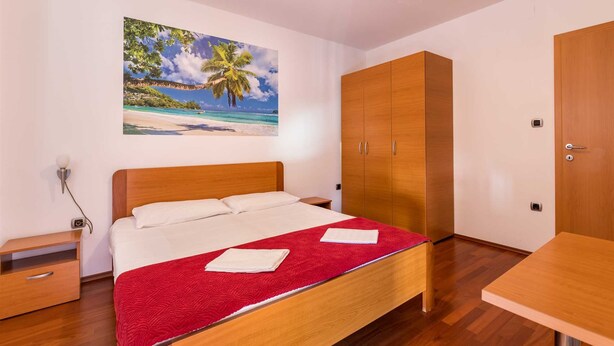 Een slaapkamer met een houten bed, een rode deken, een houten garderobe en een schilderij van een strand.