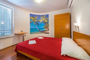 A bedroom with a bed, a wooden wardrobe, a wall-mounted light, and a window with blinds. - Apartment Nada 2 with air condition and wifi internet (Baška)