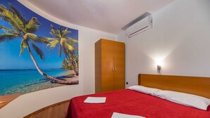 A hotel room with a bed, a wooden wardrobe, and a wall mural of a beach scene. - Apartment Nada 2 with air condition and wifi internet (Baška)