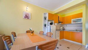 A dining area with a wooden table and chairs, a small potted plant, and a wall-mounted light fixture. - Apartment Nada 2 with air condition and wifi internet (Baška)