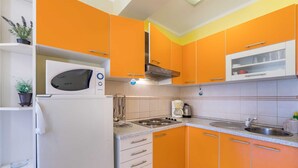 A kitchen with orange cabinets, a white refrigerator, a stove, and a microwave. - Apartment Nada 2 with air condition and wifi internet (Baška)