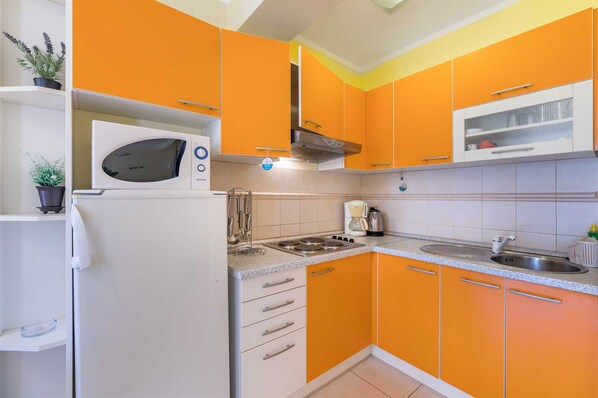 A kitchen with orange cabinets, a white refrigerator, a stove, and a microwave. - Apartment Nada 2 with air condition and wifi internet (Baška)