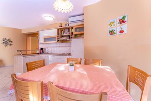 Een kleine keuken met witte kastjes, een magnetron en een spoelbak. Er staat een eettafel met een rood-wit geruit tafelkleed en zes houten stoelen.