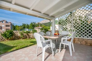 Eine überdachte Terrasse mit Tisch und Stühlen, Blick auf eine gebirgige Landschaft und ein weißes Gitterzaun.