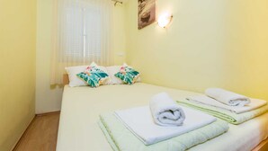 Ein Hotelzimmer mit Bett, zwei Kissen, einem Fenster mit Vorhängen, einer Wandleuchte und einem Gemälde.
