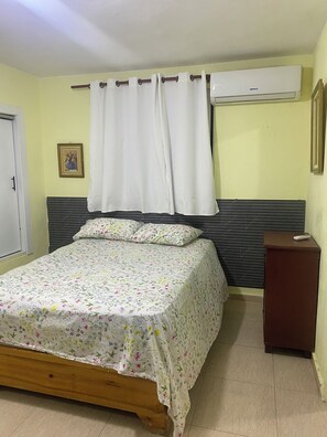 Een slaapkamer met een bed, nachtkastje, airconditioning en gordijn.