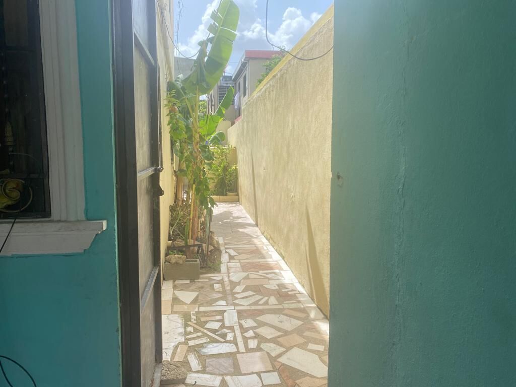Une ruelle étroite, avec un sol carrelé, un mur vert d’un côté et une fenêtre de l’autre.