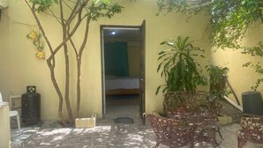 A small, enclosed outdoor area with a tiled floor, a metal table with chairs, a potted plant, and a doorway leading to a room with a bed. - Nido del patio, 40 min playa boca chica y 5 min centro de ciudad (Santo Domingo, Este)