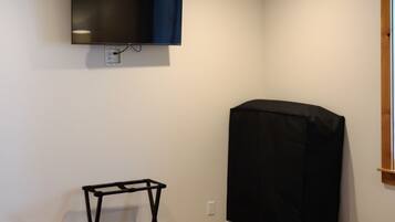 A room with a flat-screen TV mounted on the wall, a wooden floor, and a bed with a quilt.