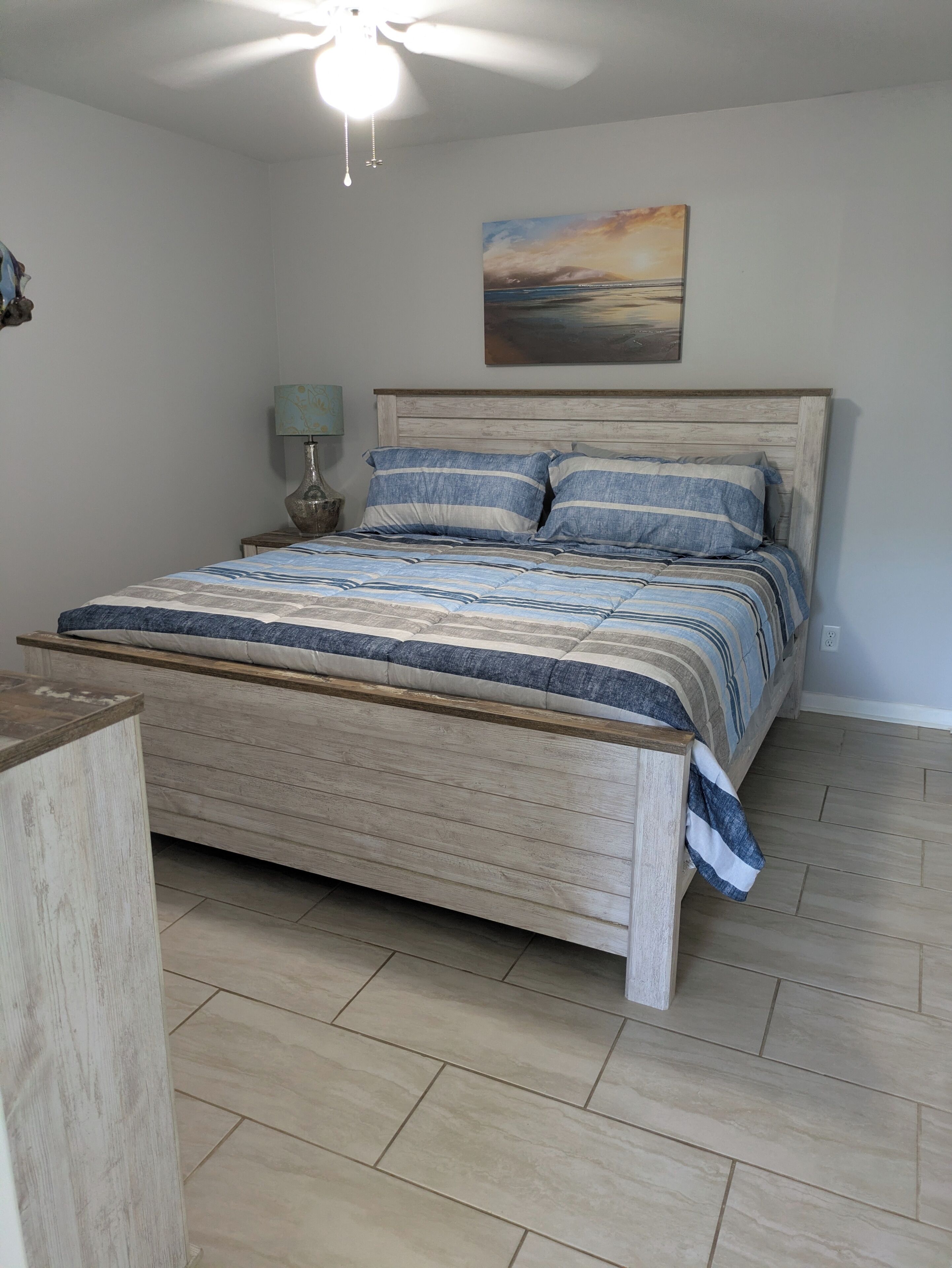 Un dormitorio con una cama de madera, una mesita de noche, una lámpara y un cuadro en la pared.