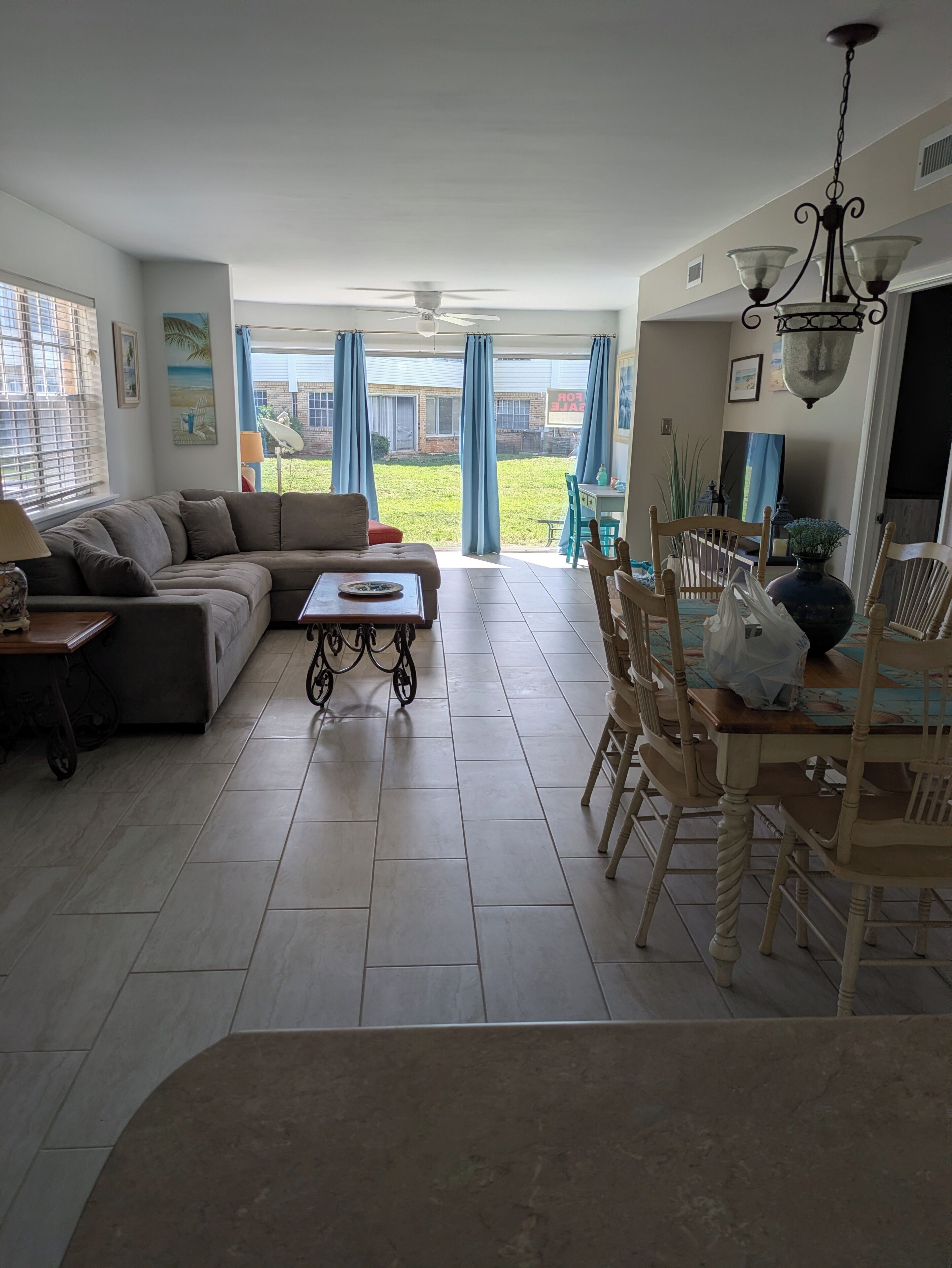 A living room with a sofa, coffee table, dining table with chairs, and a view of the backyard.