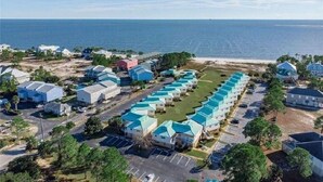 Zona residencial costera con una hilera de casas con tejados azules, un estacionamiento y una playa al fondo.