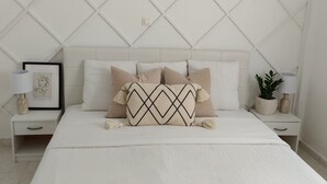 Una camera da letto ordinata con un letto, due comodini, un quadro incorniciato e due piante in vaso.
