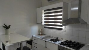 Una cucina moderna con un piano di lavoro bianco, un fornello a gas, un lavello e una finestra con persiane.