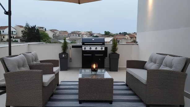 Una terrazza sul tetto con mobili in vimini, un barbecue e un braciere.