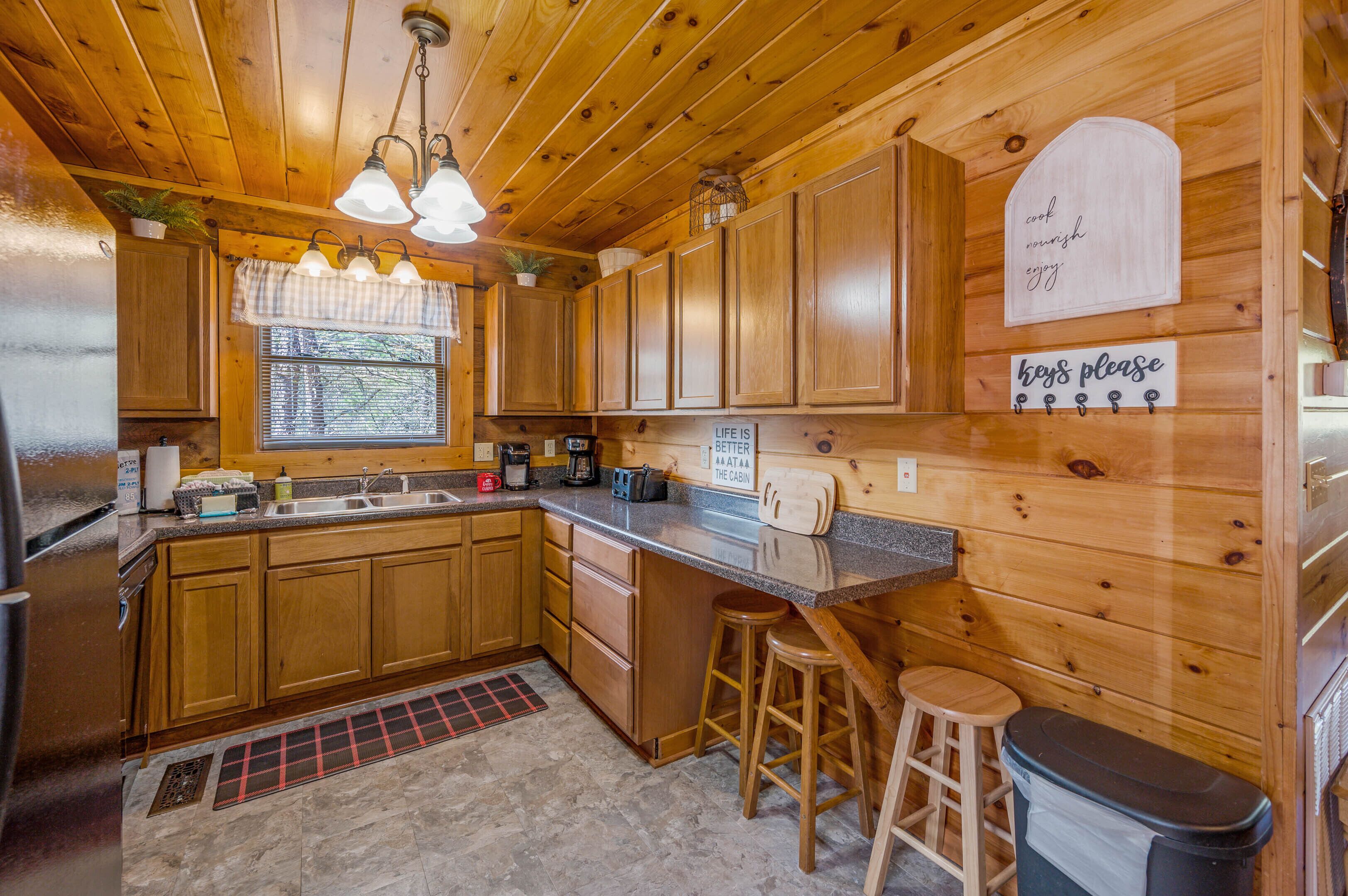 Eine Holzhütte mit einer Küche, einer Granit-Arbeitsplatte, Holzausstattung, einem Spülbecken, einer Kaffeemaschine und einem Schild mit der Aufschrift 'LIFE IS BETTER AT THE CABIN'.