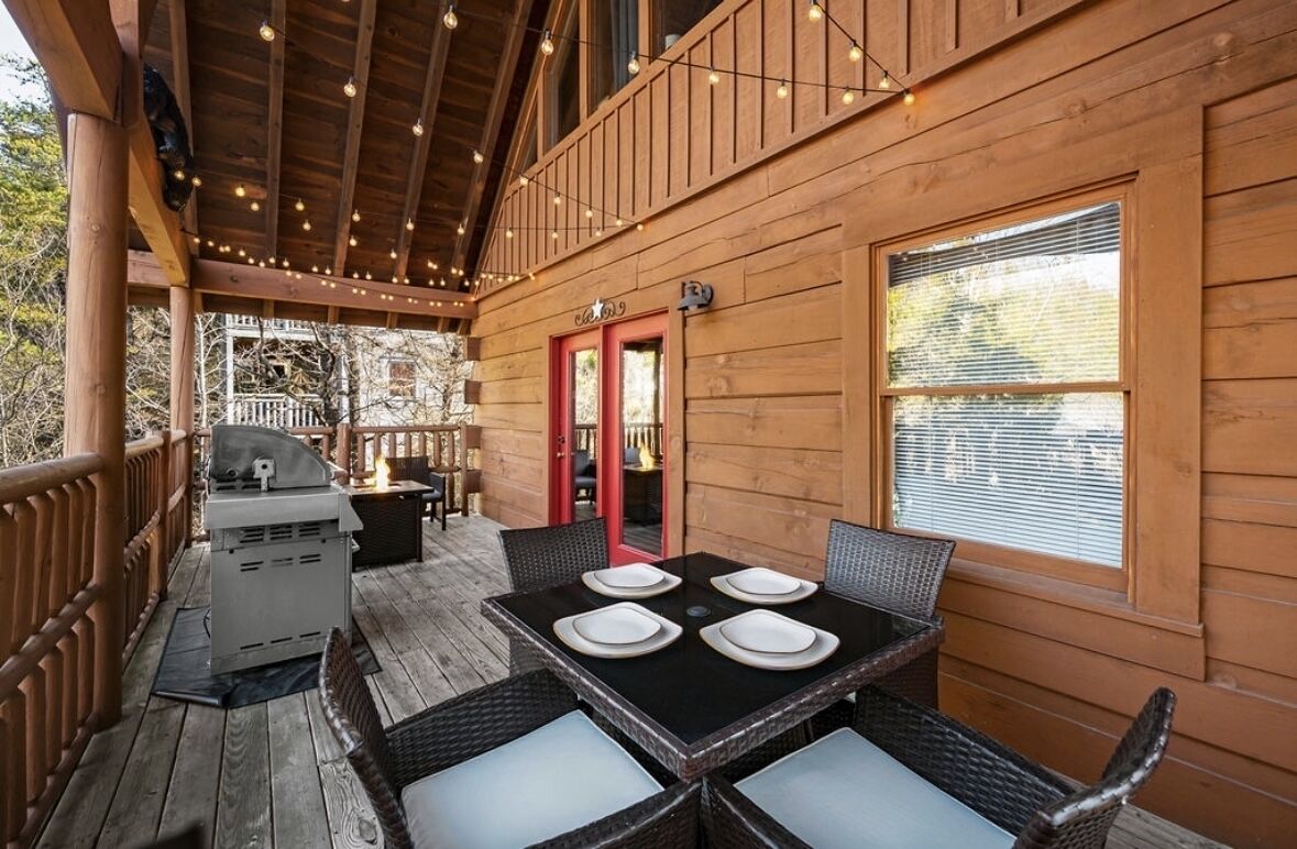 Una terraza de madera con una parrilla, una mesa de comedor con sillas y una puerta roja.