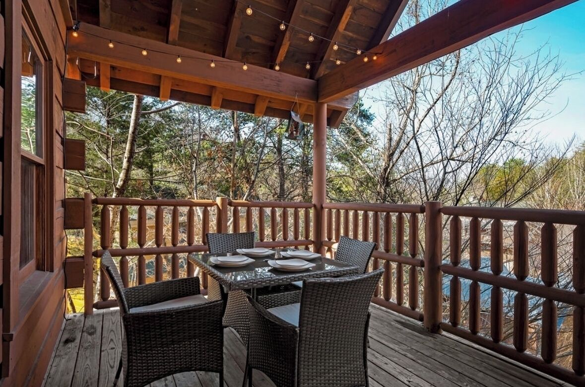 Une terrasse en bois, agrémentée d’une table et de chaises, entourée d’une balustrade en bois, et offrant une vue sur un paysage naturel.