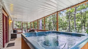 Ein Whirlpool in einem überdachten Außenbereich mit Holzterrasse, umgeben von Bäumen.
