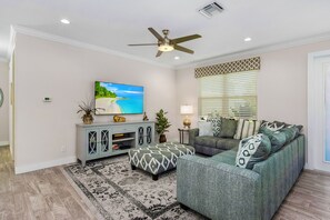 A living room with a sofa, ottoman, TV, and ceiling fan. - Waterfront Cape Coral Villa w/ Heated Pool, 4 Bedrooms, Pet-Friendly (Cape Coral)