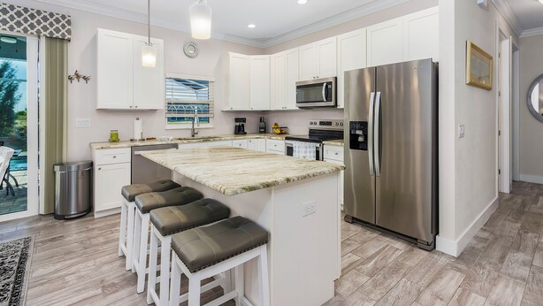 A modern kitchen with white cabinets, stainless steel appliances, and a central island with bar stools. - Waterfront Cape Coral Villa w/ Heated Pool, 4 Bedrooms, Pet-Friendly (Cape Coral)