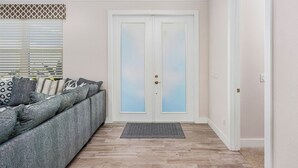 A hallway with a grey sofa, patterned cushions, a frosted glass door, and a wooden floor. - Waterfront Cape Coral Villa w/ Heated Pool, 4 Bedrooms, Pet-Friendly (Cape Coral)