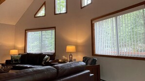 A cozy living room with a dark brown leather sofa, a small side table with a lamp, and a large window with blinds. - STOP SCROLLING & CHECK OUT OUR REVIEWS. NO ADDITIONAL FEES TO ENTER COMMUNITY (Pocono lake)