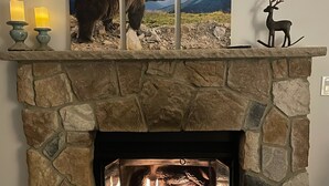 A stone fireplace with a fire, a bear and deer artwork above it, and two lit candles on the mantel. - STOP SCROLLING & CHECK OUT OUR REVIEWS. NO ADDITIONAL FEES TO ENTER COMMUNITY (Pocono lake)