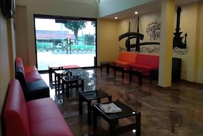 A hotel lobby with a red sofa, black chairs, a glass table, and a mural on the wall.