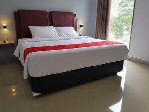 A hotel room with a large bed, a red accent on the bedspread, and a view through a window.