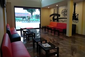 A hotel lobby with a red sofa, black chairs, a glass table, and a mural on the wall. - MJ s Hotel (Jambi)