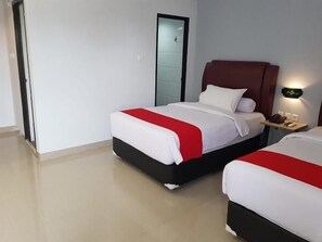 A hotel room with two beds, each with a red and white bedspread, a wooden nightstand with a lamp, and a door leading to another room. - MJ s Hotel (Jambi)