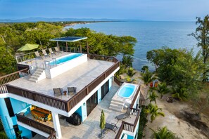 A modern two-story building with a rooftop pool, a separate hot tub, and a dining area with outdoor seating.