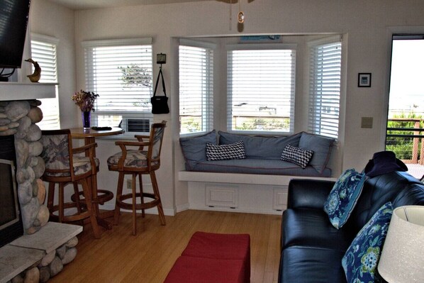 A living room with a stone fireplace, a bay window seating area, a dining table with chairs, and a leather sofa. - Great deck with gorgeous ocean view! (Cambria)