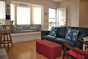 Un salon comprenant un canapé, un banc, un pouf rouge et une chaise en bois.