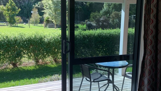 A room with a sliding glass door leading to an outdoor deck with a table and chairs. - Rural cottage        (Tuamarina)