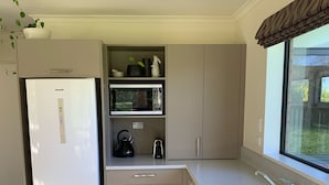A compact kitchen with a built-in refrigerator, microwave, kettle, and stove. - Rural cottage        (Tuamarina)